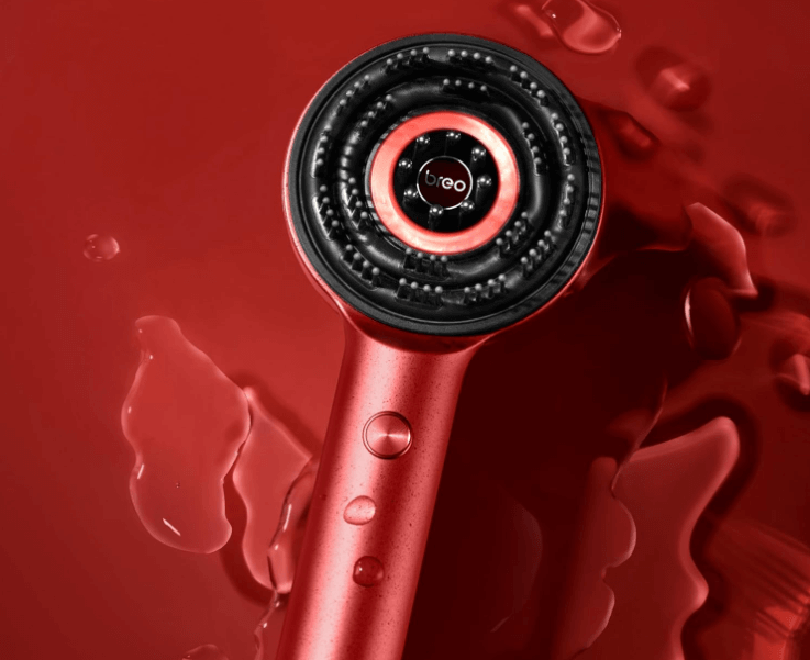 BreoRelief scalp massager with red handle and black massage head on a wet red surface, showcasing its waterproof design.